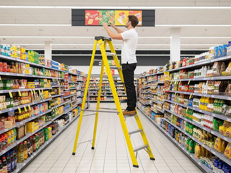 Worker using a stepladder in a workplace aisle