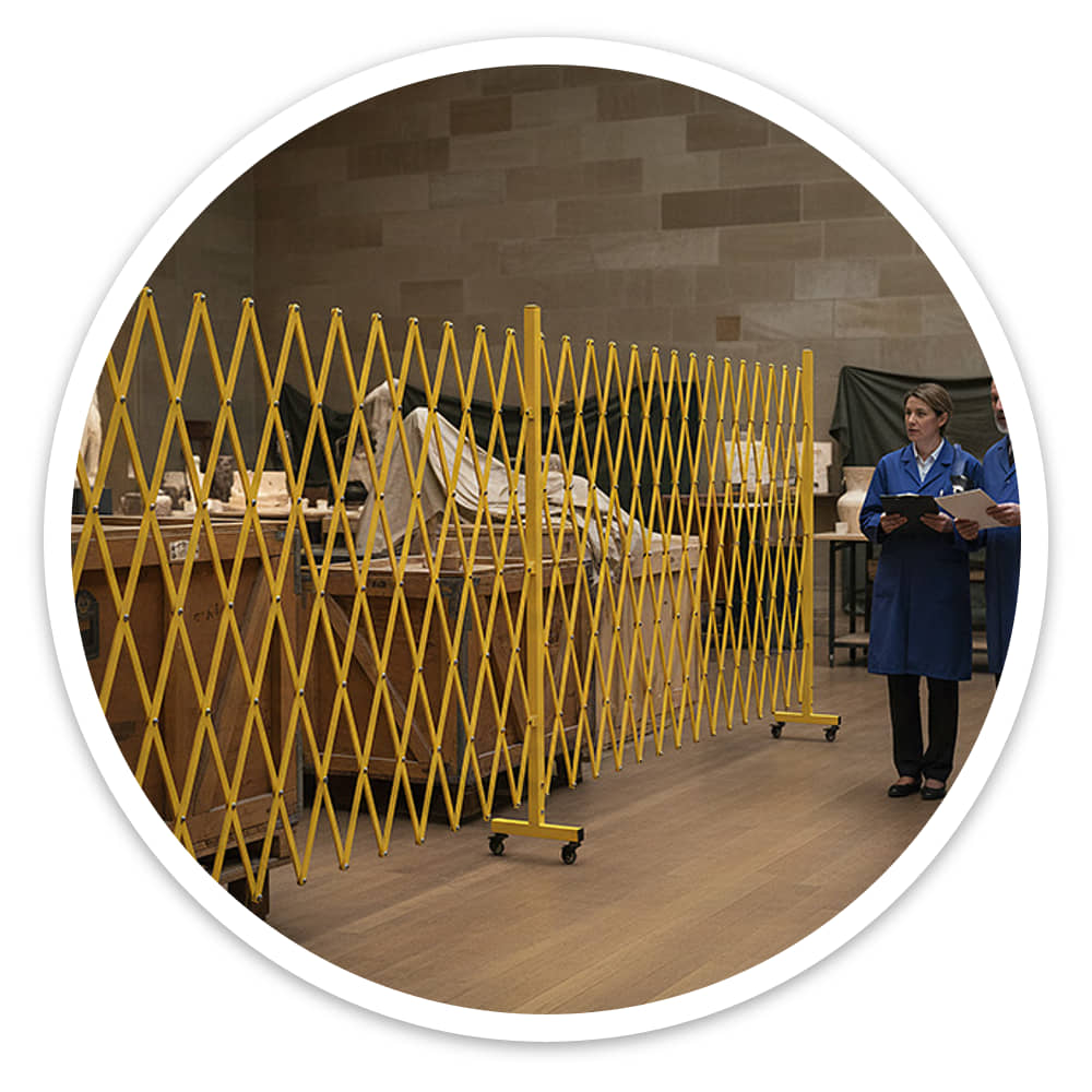 Two staff talking beside the yellow Extra Large Expandable Barrier, with the room visible through its lattice