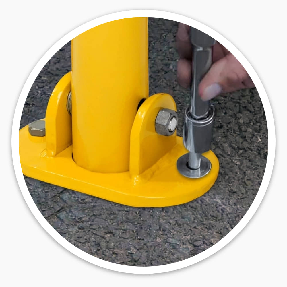 Fixing bolt being tightened through the base plate of a yellow folding parking post on tarmac