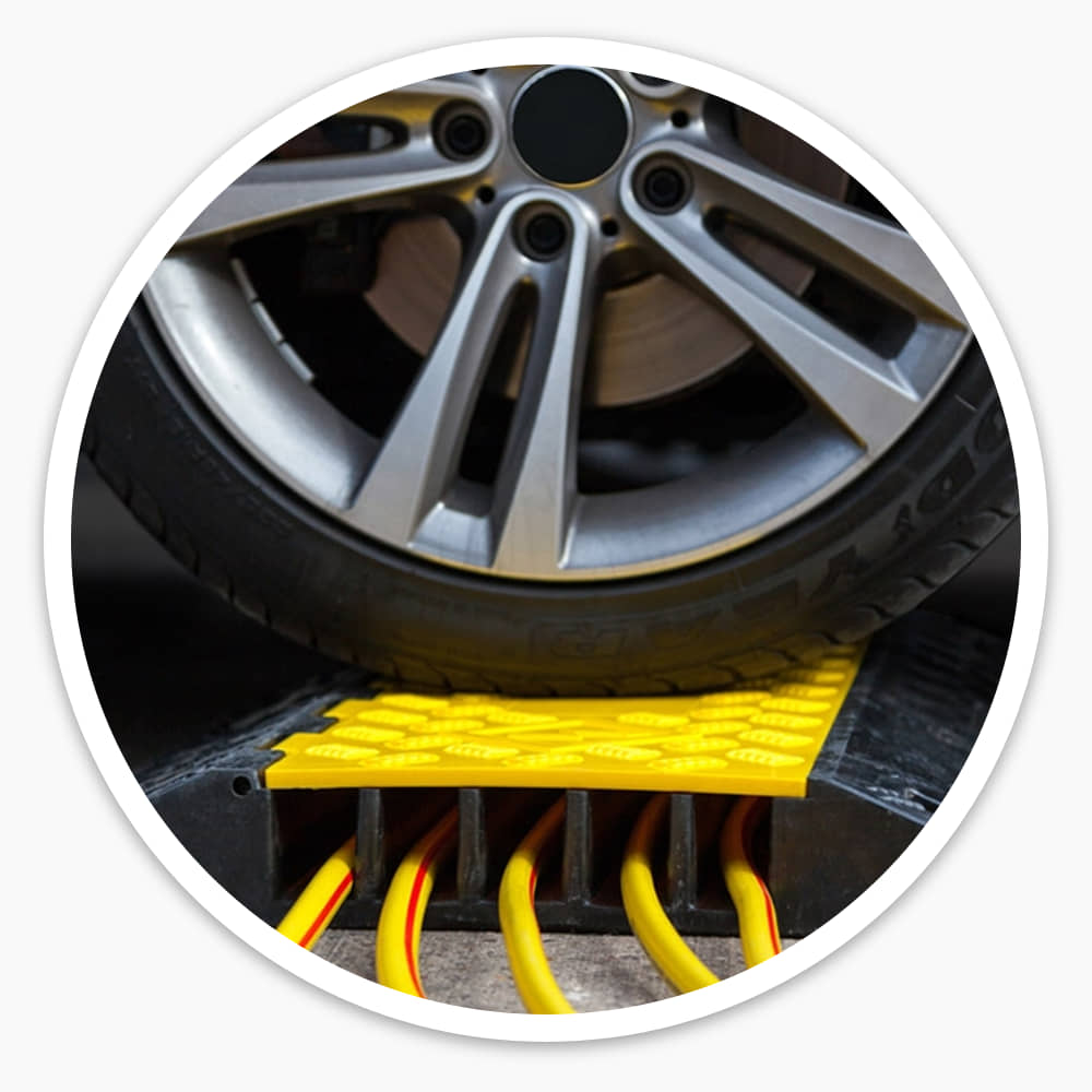Car wheel resting on a 5 channel cable ramp with yellow cables running through its five channels