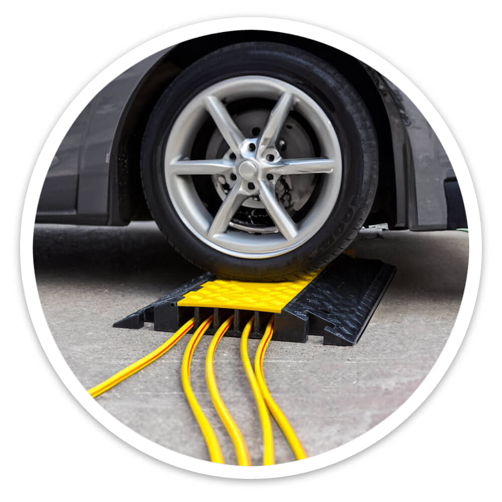 Car tyre driving over a 5 channel cable ramp with rubber base protecting yellow cables outdoors