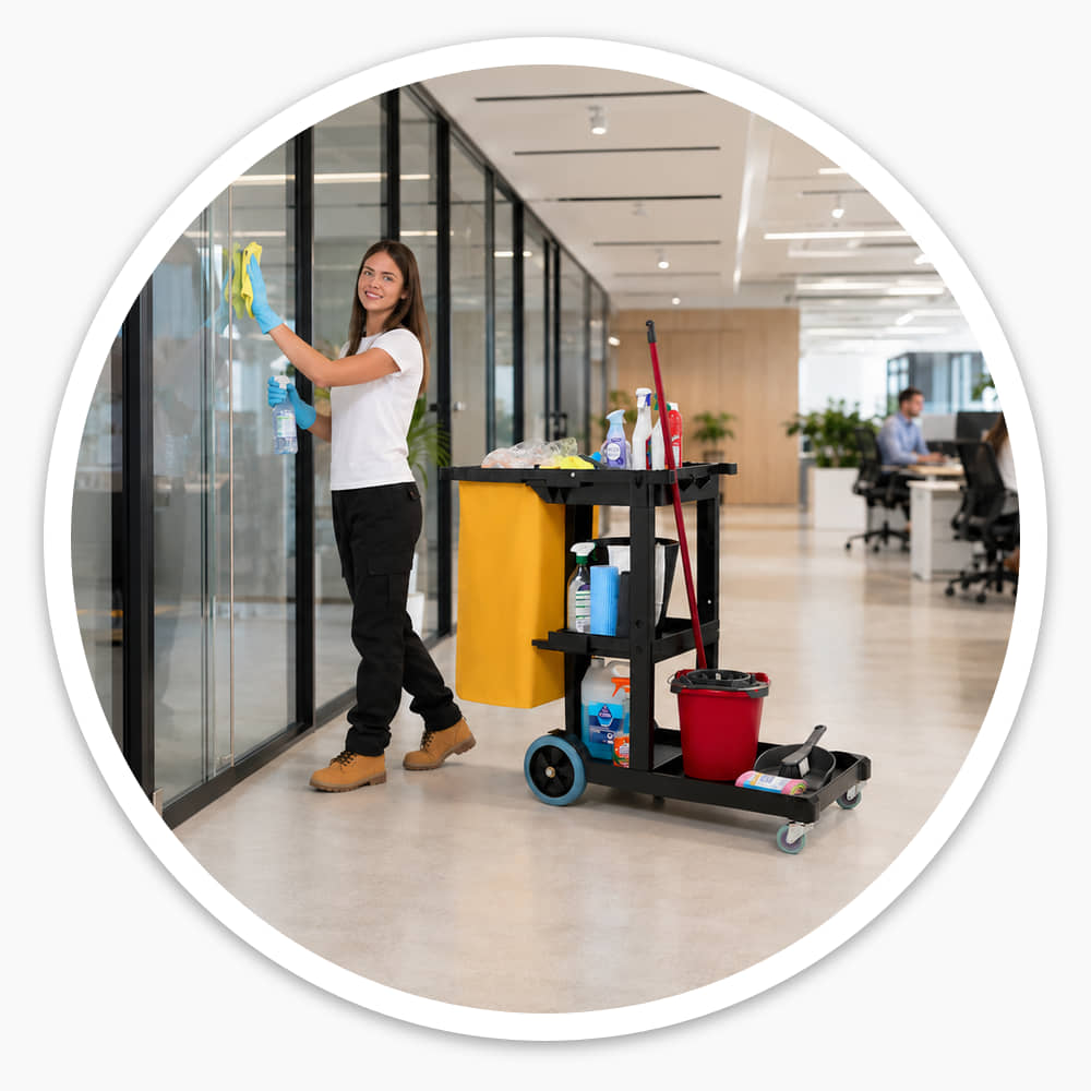 Cleaner wiping office glass beside the Economy Cleaning Cart with its yellow waste bag and trays of supplies
