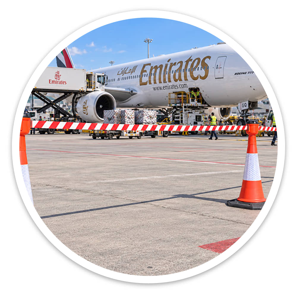 Red and white retractable cone barrier cordoning off an outdoor airport apron beside an aircraft