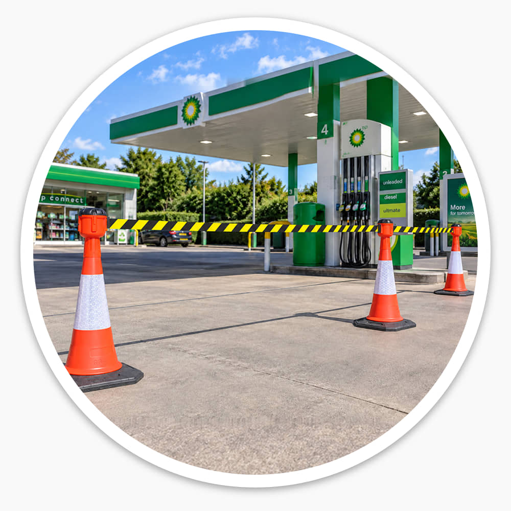 Yellow and black retractable cone barrier belts stretched across a petrol station forecourt lane