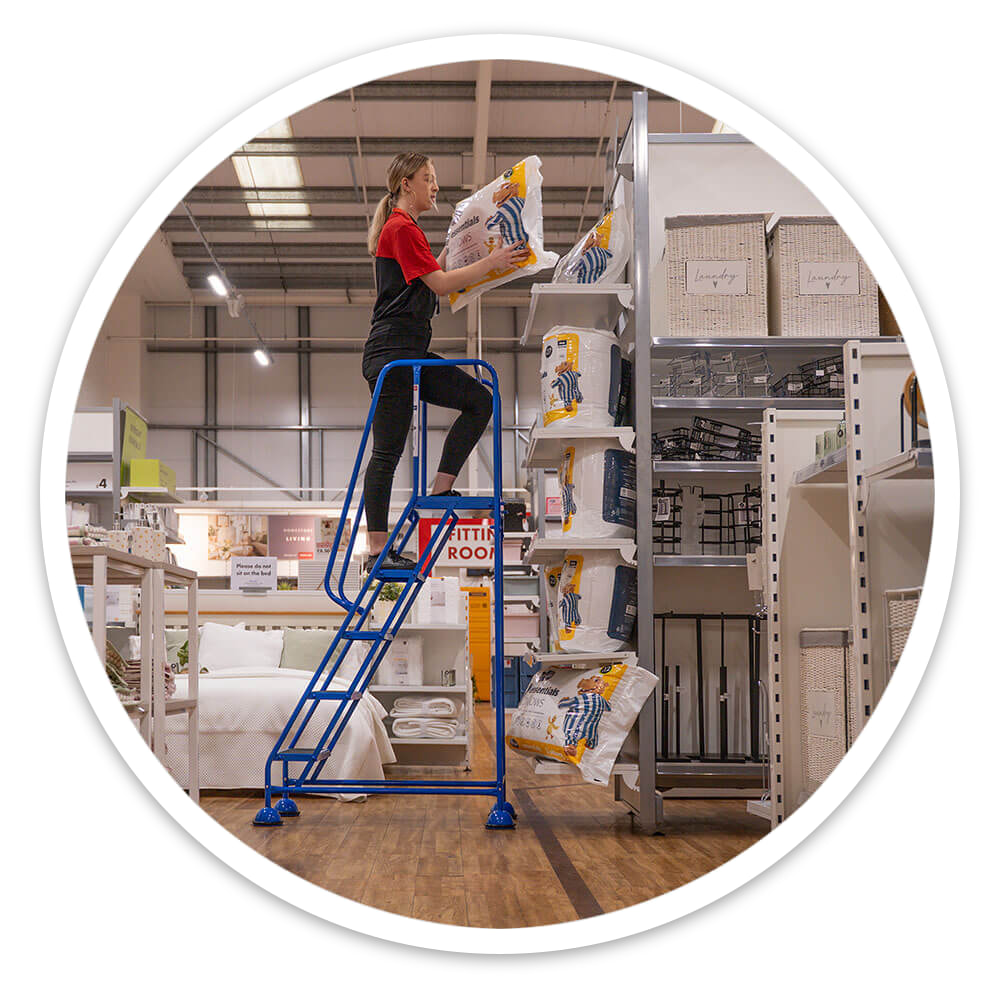 Retail worker at platform height on the 5 Tread Mobile Safety Steps reaching high stock on racking