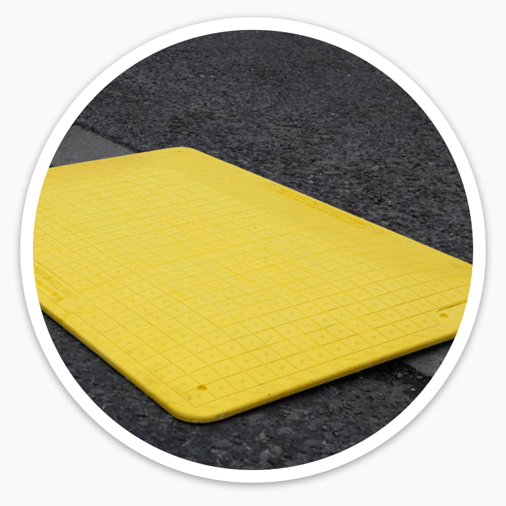Low-profile yellow Pedestrian Hole Cover with chamfered edges lying on a road surface beside the kerb