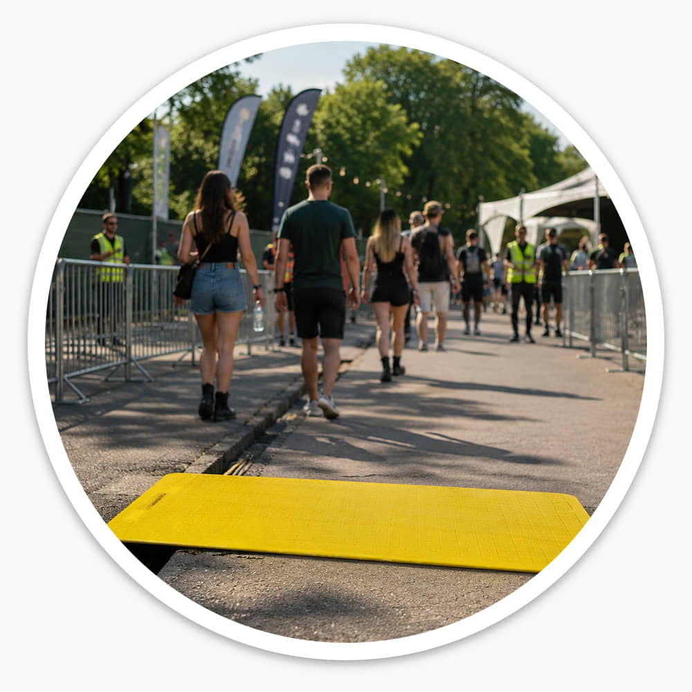 Yellow Pedestrian Hole Cover laid over a trench at an outdoor event entrance, with a steward nearby