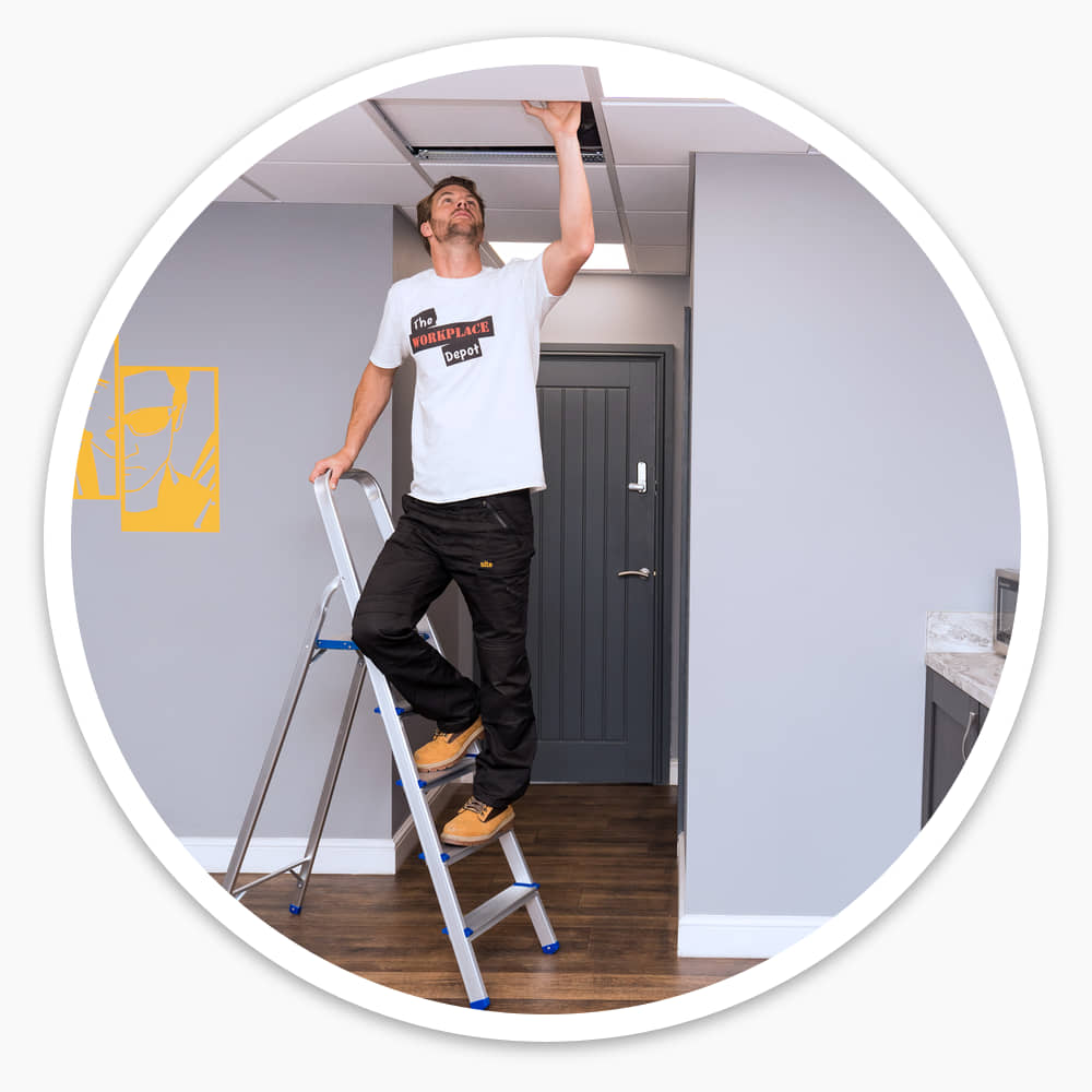 Man on a 5 tread lightweight aluminium step ladder reaching up to a ceiling tile in an office kitchen