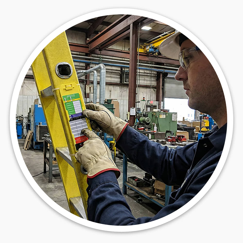 Worker in a factory checking a ladder inspection tag fixed to a yellow extension ladder