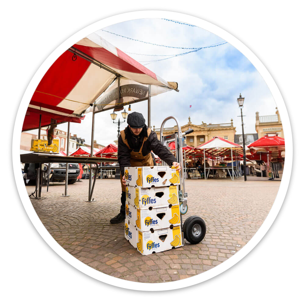 Trader with boxes of bananas stacked on the 2-in-1 Sack Truck used upright as a sack truck in a market square