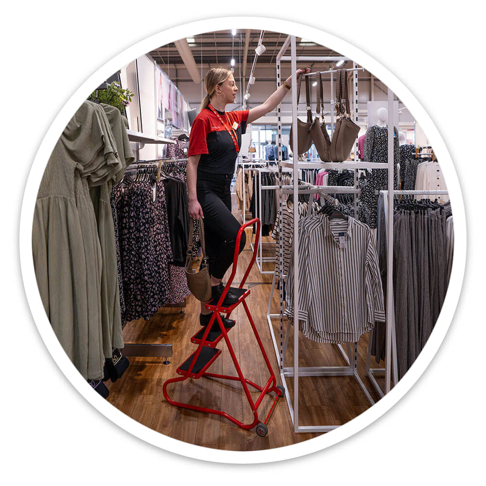 Shop assistant on the 3 Tread Wheelalong Mobile Steps handling stock on a high clothing rail