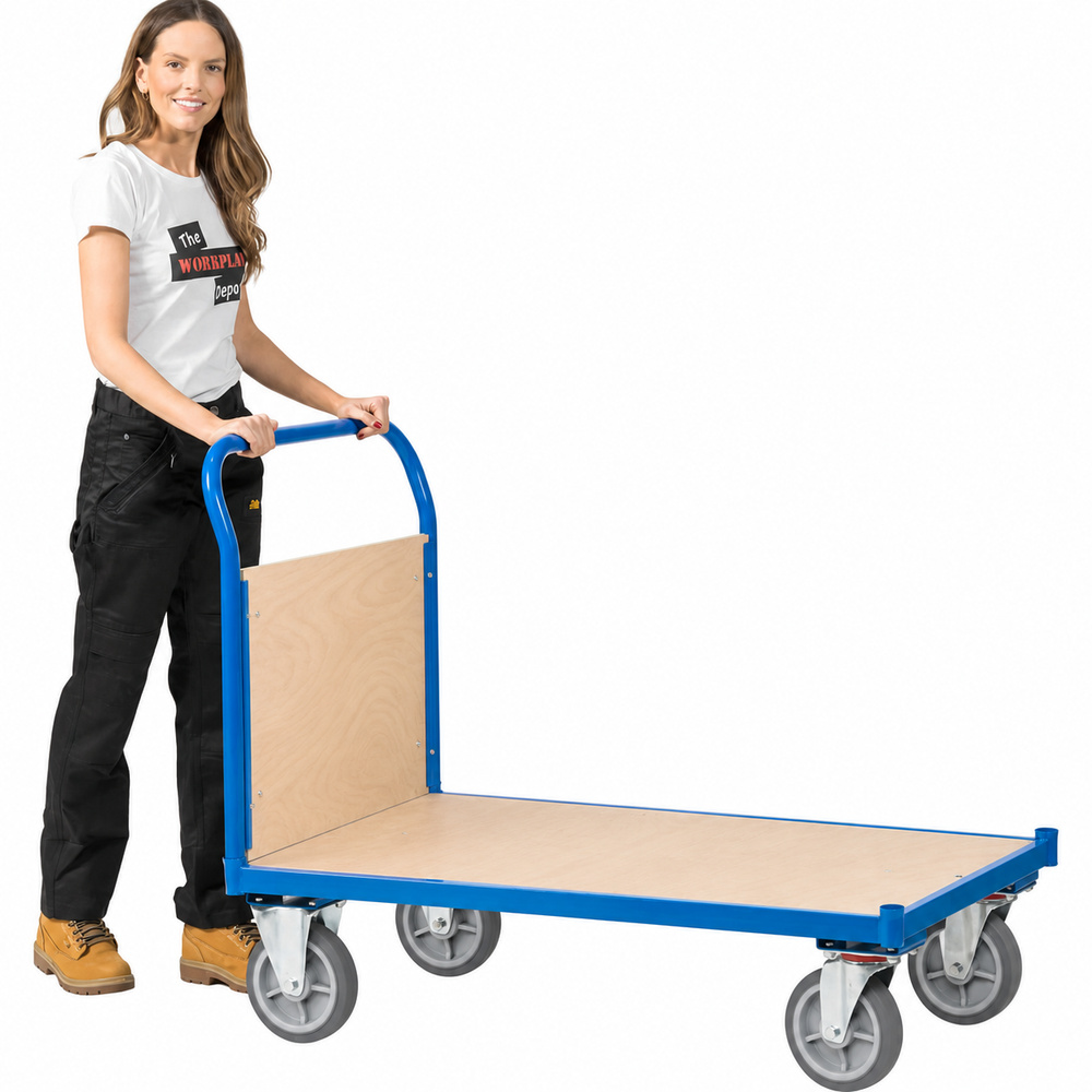 Woman pushing a blue flatbed trolley with a push handle, plywood deck and end panel, and four grey rubber wheels